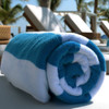 A rolled beach towel in turquoise and white stripes, resting on a lounge chair by the pool.