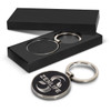 A round silver key ring with a black, textured surface, presented in a sleek black box.