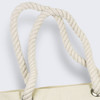 A close-up of the twisted, cream-coloured rope handles of a tote bag featuring silver eyelets.