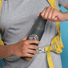 A drink bottle in matte black with a cork base, held by a person wearing a grey shirt and yellow backpack.