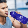 A drink bottle in vibrant purple with a logo, held by a person during a workout.