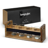 A wooden taster tray with a sleek black band holds four clear glass containers, packaged in a black box.