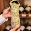 A drink bottle holder with a woven, straw-like pattern in natural tones, featuring a black top and branding.