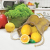 A jute net produce bag filled with lemons, accompanied by a cut lemon and a bowl of greens.