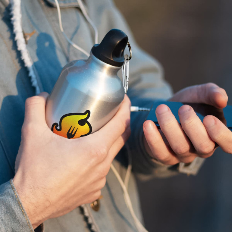 A drink bottle in silver with a colourful logo, held by a person wearing a hoodie while using a mobile device.