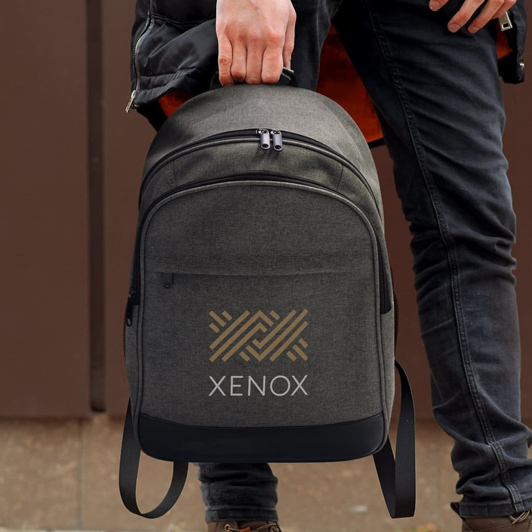 A grey backpack with a logo, being held by a person wearing dark clothing.
