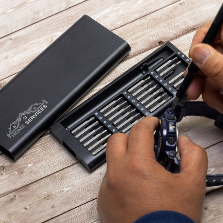 A black screwdriver set with multiple bits and a case, being used on a watch by a person.