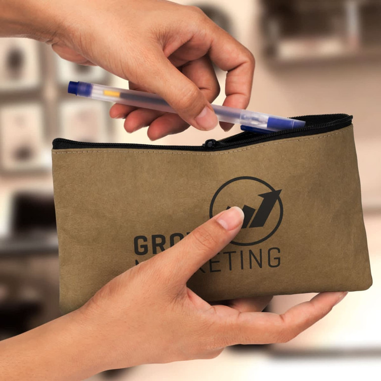 A Kraft pencil case in earthy tones, being held open with a pen being inserted. It features a logo on the front.