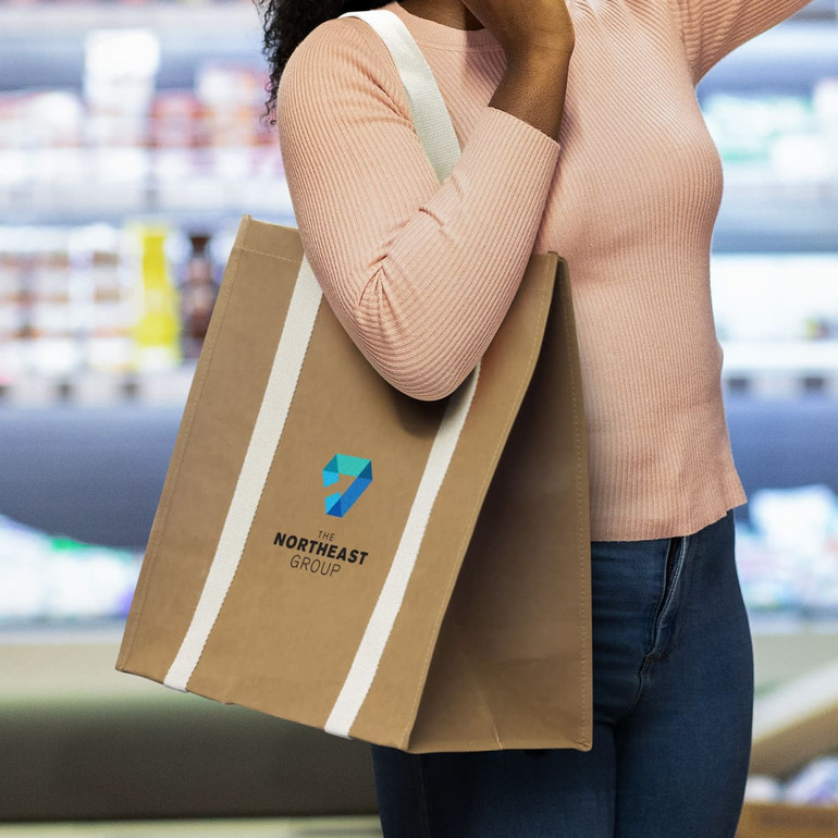A person holding a brown Kraft tote bag with white straps and a logo on the front.