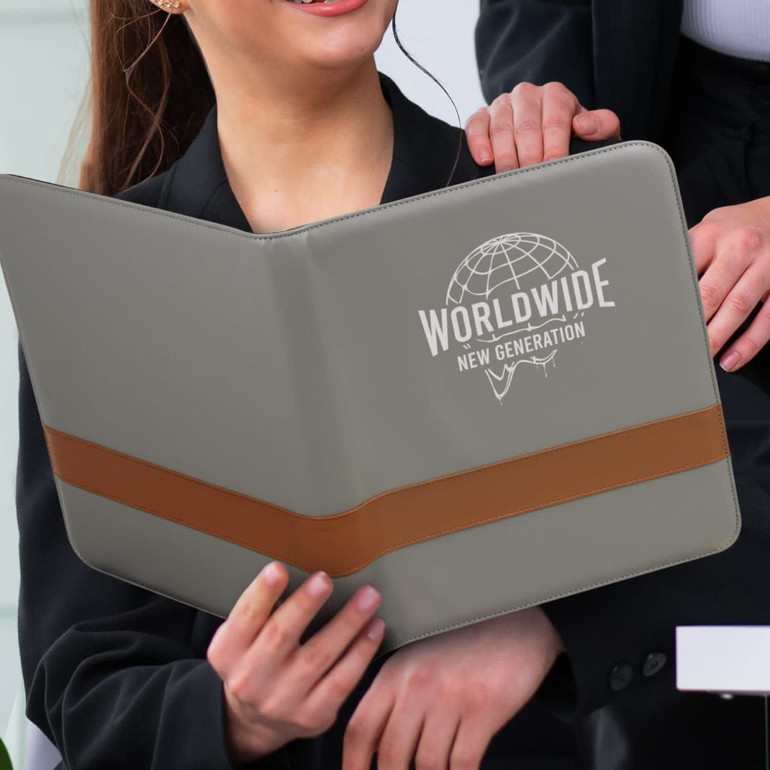 A grey portfolio with a brown strap, held by a person, featuring a logo on the front.