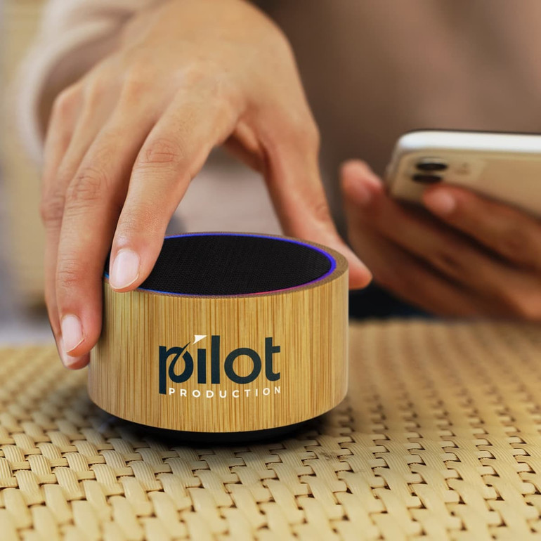 A bamboo Bluetooth speaker with a circular design and a textured surface, featuring a logo on the front.
