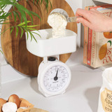Person weighing flour on white mechanical kitchen scale