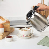 Stainless steel electric kettle with black handle, next to a cup of tea with lemon slice.
