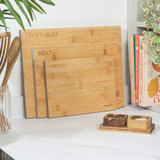 Set of three bamboo chopping boards labelled for vegetables, meat, and fruit on kitchen counter.