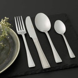 Four-piece stainless steel cutlery set with fork, knife, dessert spoon and teaspoon on slate.