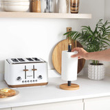 Hand placing kitchen roll on black and wood holder beside white toaster on worktop