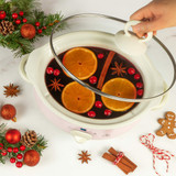 Pink slow cooker with mulled wine, orange slices and spices, shown with festive decor.
