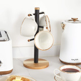 Set of four cream stoneware mugs with brown rim on black and wood mug tree, kitchen counter.