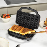 Black waffle maker with two golden waffles on kitchen worktop, hand lifting one waffle.