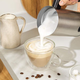 Stainless steel electric milk frother with black handle, shown upright.