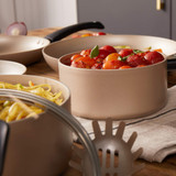 Set of beige non-stick saucepans and frying pan with pasta and tomato sauce, kitchen setting