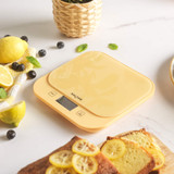 Yellow digital kitchen scale on countertop with lemons, blueberries and lemon loaf
