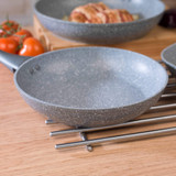Grey non-stick frying pan on metal trivet, angled view, suitable for induction hobs