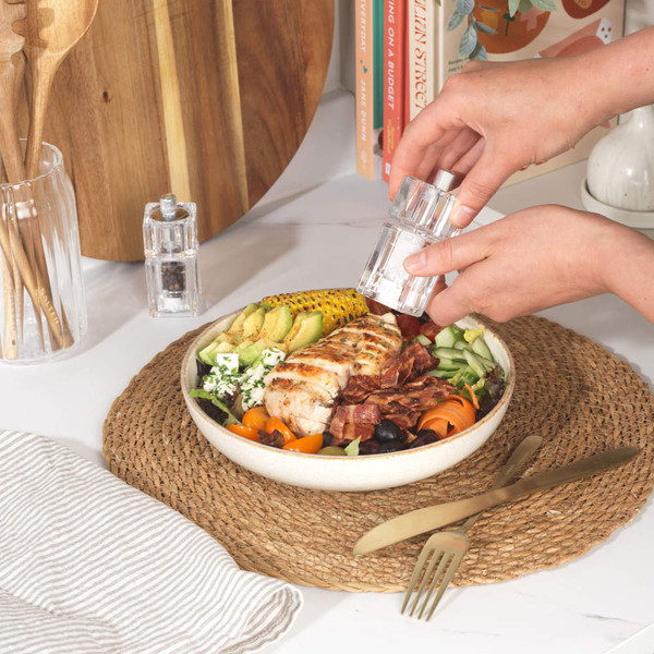 Bowl of grilled chicken salad with vegetables on dining table, hand using salt grinder