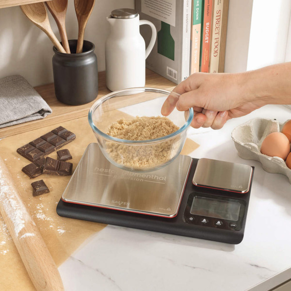 Digital kitchen scale with brushed metal surface in open drawer beside wooden utensils