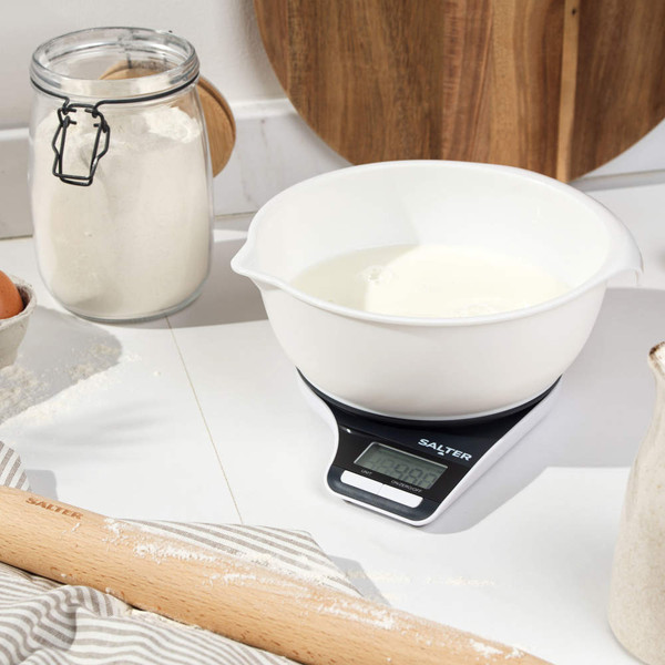 Digital kitchen scale with white mixing bowl, flour and baking tools on worktop