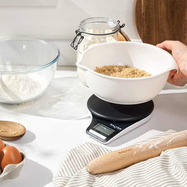 Digital kitchen scale weighing brown sugar in white mixing bowl