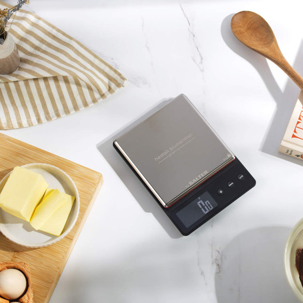 Stainless steel digital kitchen scale with display, shown on worktop with butter and utensils