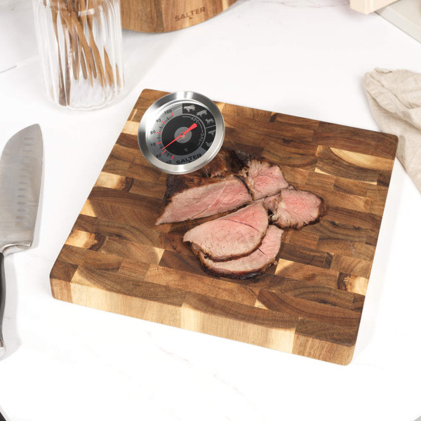 Meat thermometer showing temperature in cooked beef joint on wooden board