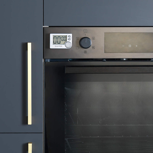 Built-in oven in matte black kitchen with brass handles, timer visible