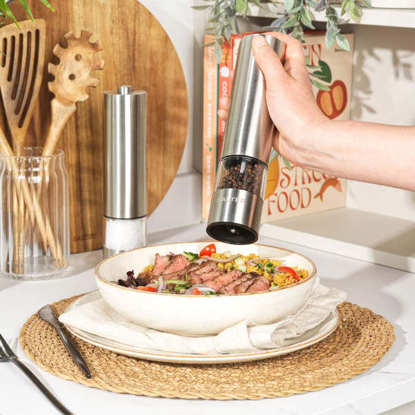 Stainless steel electric salt and pepper grinders in use over a salad bowl