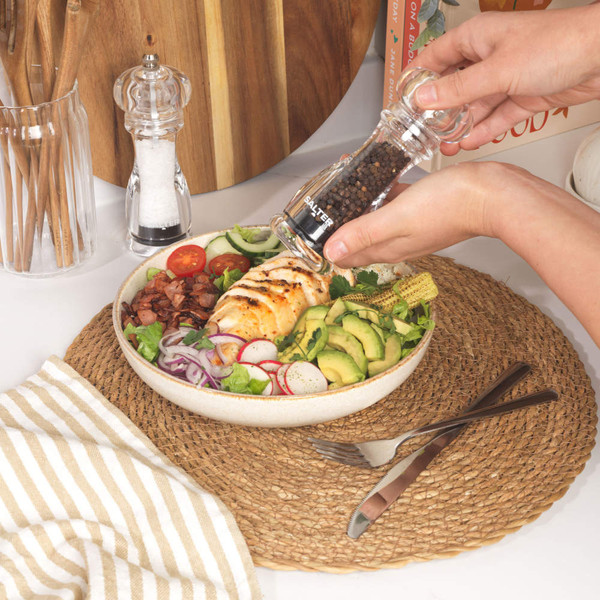Hand seasoning grilled chicken salad with a Salter pepper mill on kitchen table.