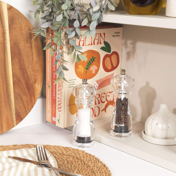 Salt and pepper grinders with clear acrylic bodies on a kitchen shelf
