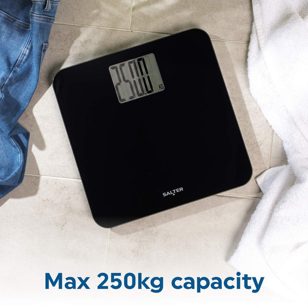 Black digital bathroom scale on tiled floor, near jeans and white towel