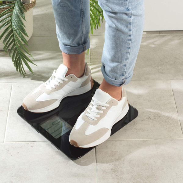 Person in light trainers and jeans standing on digital bathroom scale