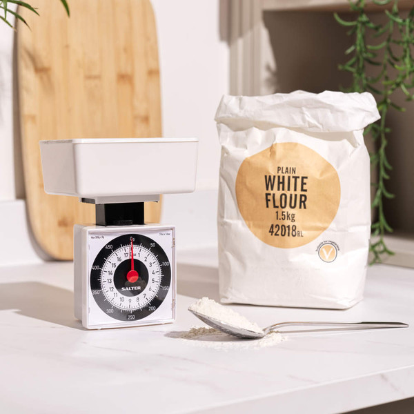 1.5kg bag of plain white flour beside kitchen scales and spoon of flour, on countertop