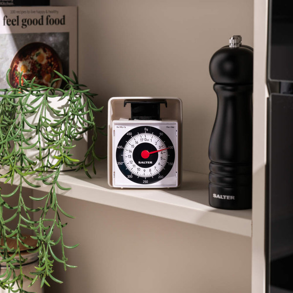 White Salter mechanical kitchen scale on shelf, shown next to black pepper grinder.
