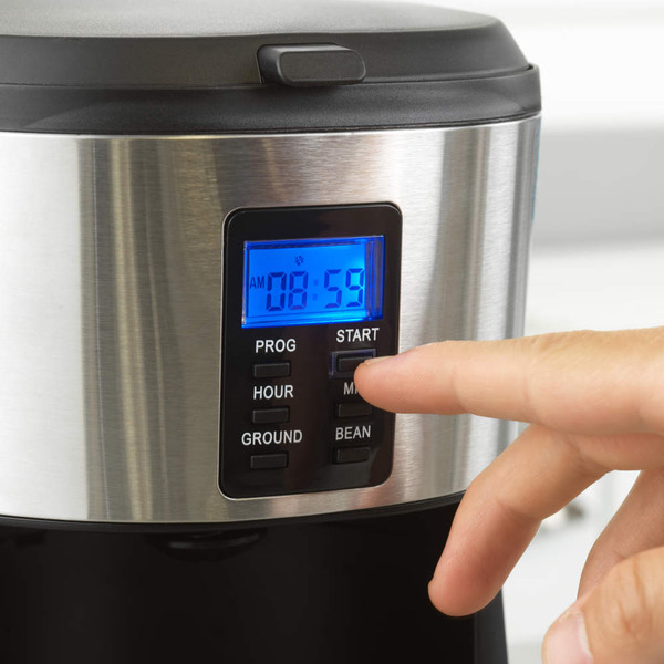 Hand pouring coffee beans into open black coffee machine, filter and scoop beside.