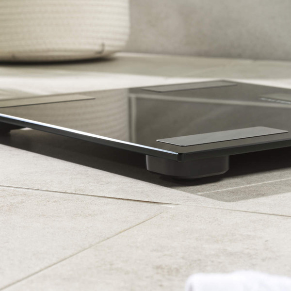 Black glass digital bathroom scale on tiled floor, showing low side profile.
