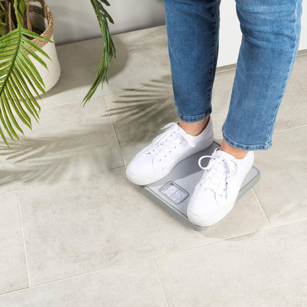 Person in blue jeans and white trainers standing on a grey mechanical bathroom scale