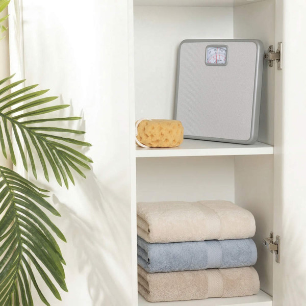 Silver mechanical bathroom scale on shelf beside sponge and folded towels