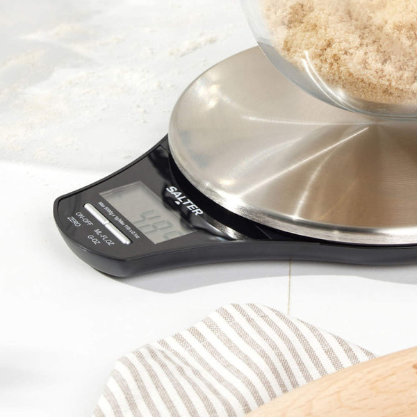 Digital kitchen scale with stainless steel platform in use weighing brown sugar
