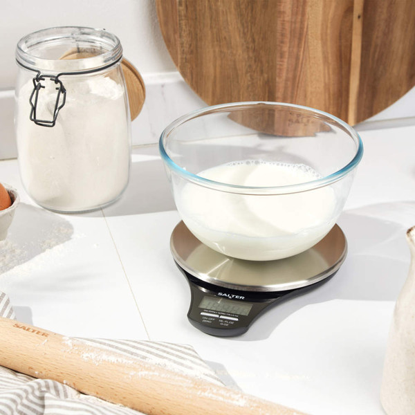 Kitchen scene with hand weighing brown sugar in glass bowl on digital Salter scale