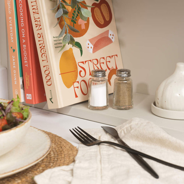 Salt and pepper shakers beside cookbooks and table setting with salad bowl