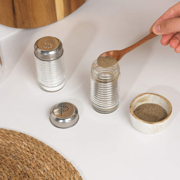 Glass salt and pepper shakers with metal lids, one being filled with ground pepper