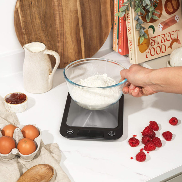 Digital kitchen scale with bowl holding butter, sugar and egg for baking, shown on zero.